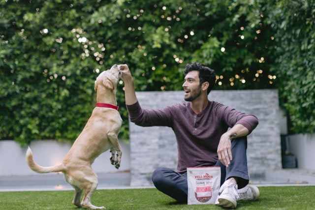 A man smiles while feeding his pet with a bag of dog treats